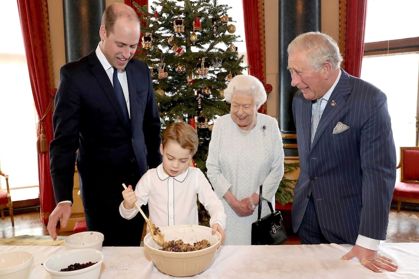 Queen Elizabeth, Prince Charles, Prince William stand around and Prince George as he stirs Christmas pudding mixture.