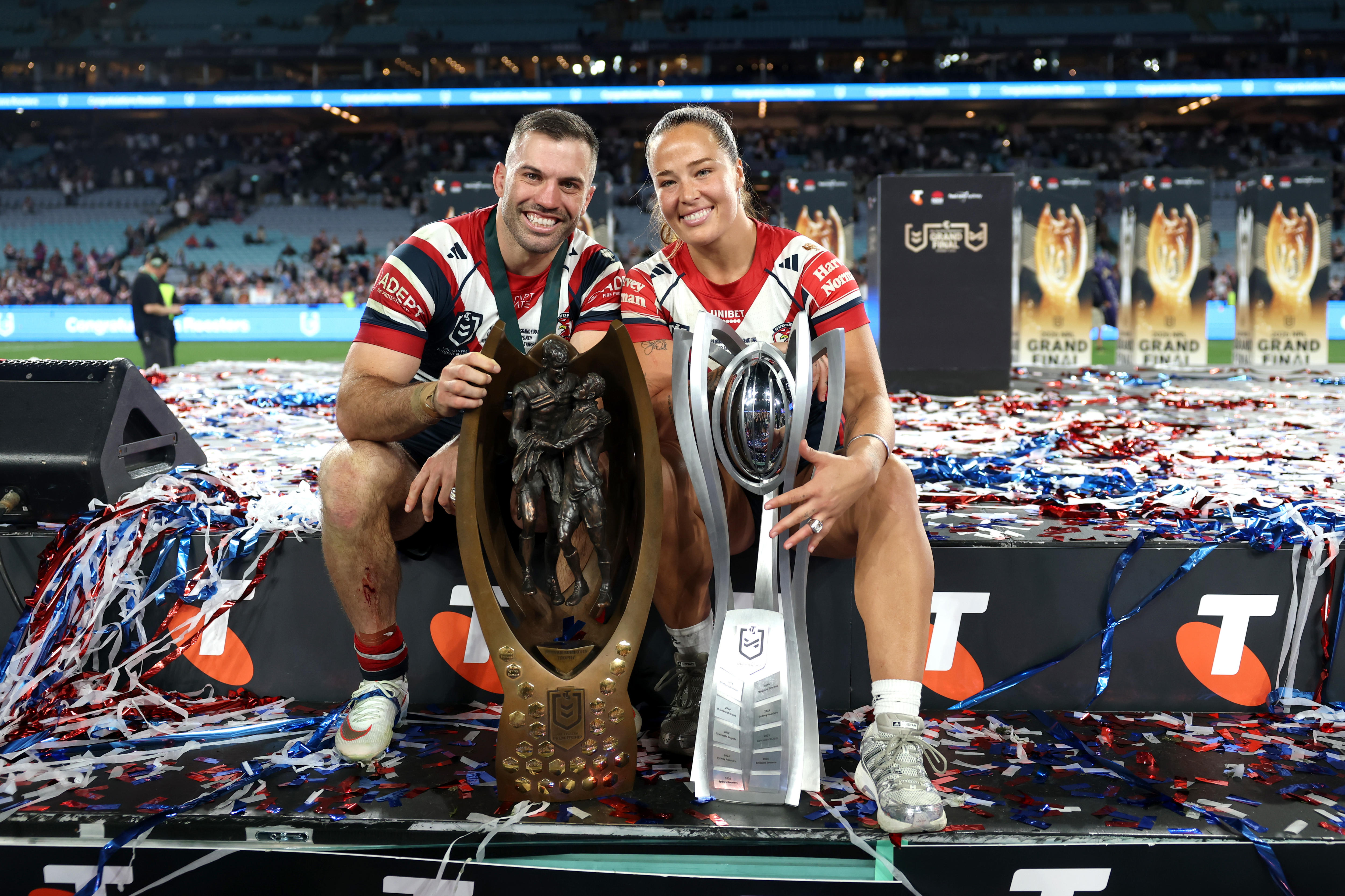James Tedesco and Isabelle Kelly sit and smile with their premiership trophies