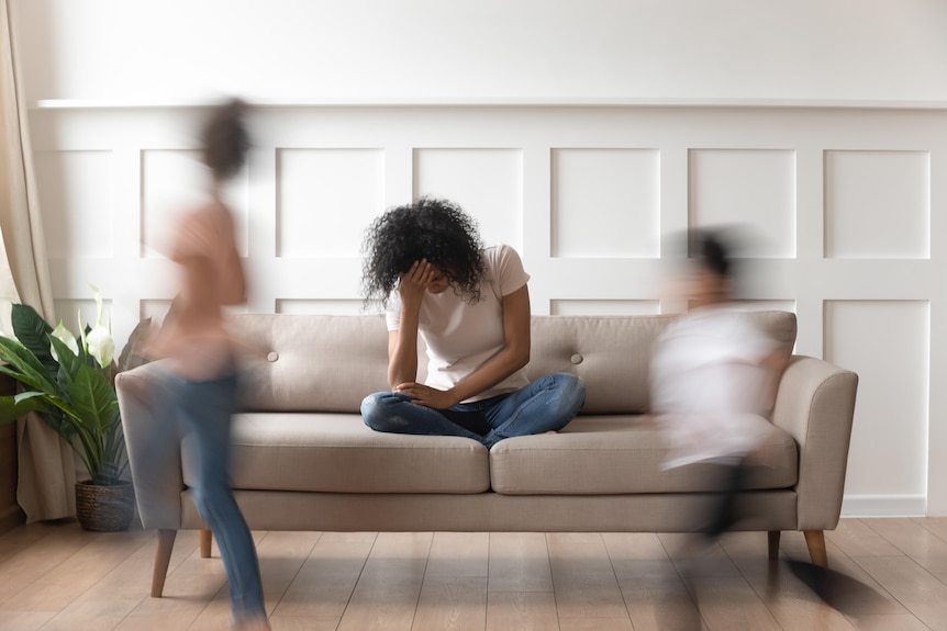  upset black mother holds hands in face as two children run around the couch