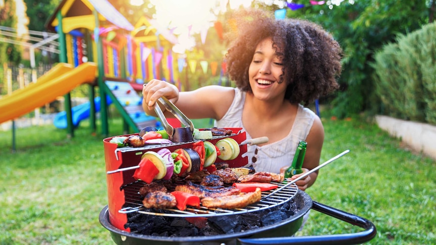 A woman cooking on a barbecue in the backyard.