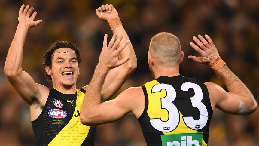 Two AFL teammates raise their hands to high-five each other in celebration after a goal.