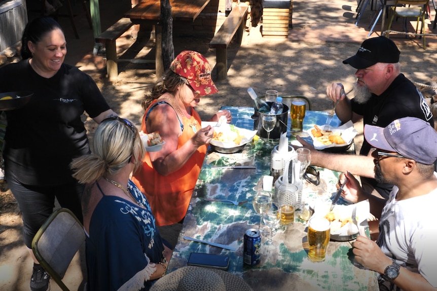 A waitress delivers food to four diners in an al fresco area of a restaurant