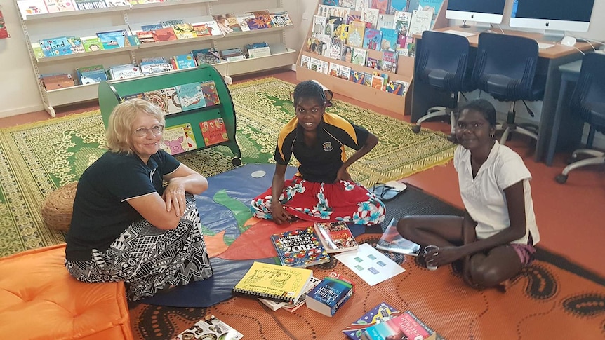 A grupo of three women sitting in a remote library surrounded by books.