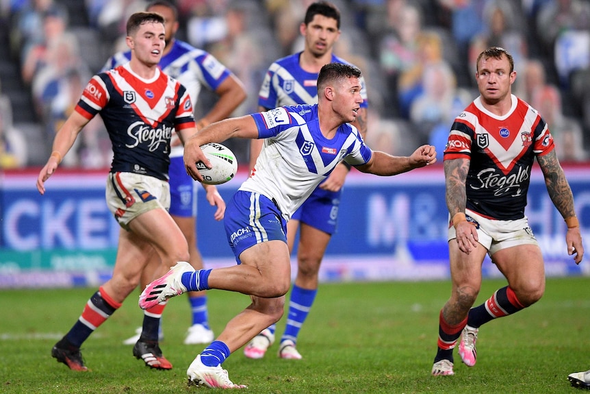 A Canterbury Bulldogs NRL player holds the ball on his right hand as he runs at the Sydney Roosters defence.