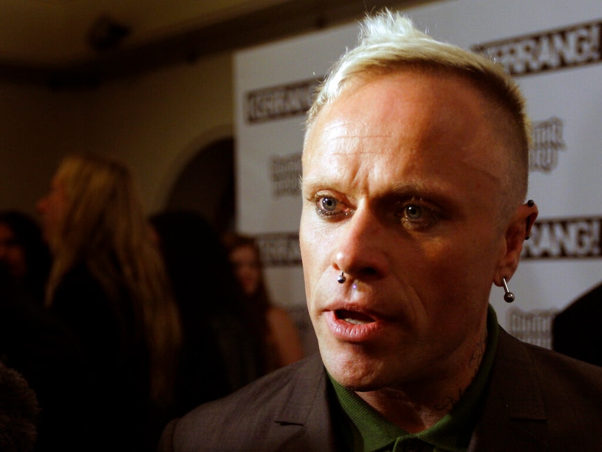 A man with blonde hair and blue eyes with a bar piercing in his nose and ear during an interview