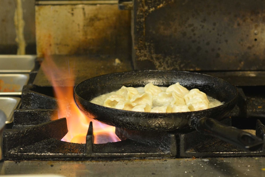 Dumplings fry in a pan over a hot flame.