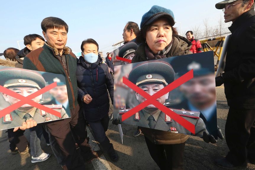 Family members of victims of the sunken South Korean naval ship Cheonan hold defaced portraits of Kim Yong Chol