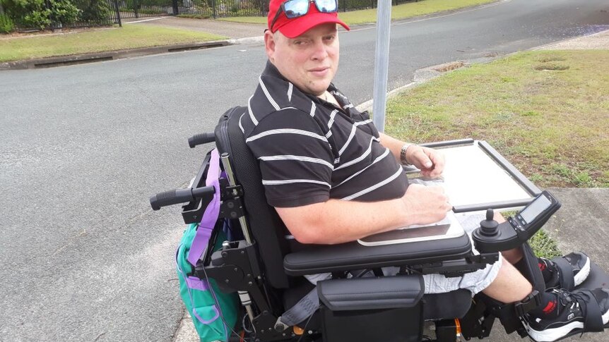 Nigel Webb sits in his motorised wheelchair on the footpath of a suburban street, which is barely wide enough for his chair.