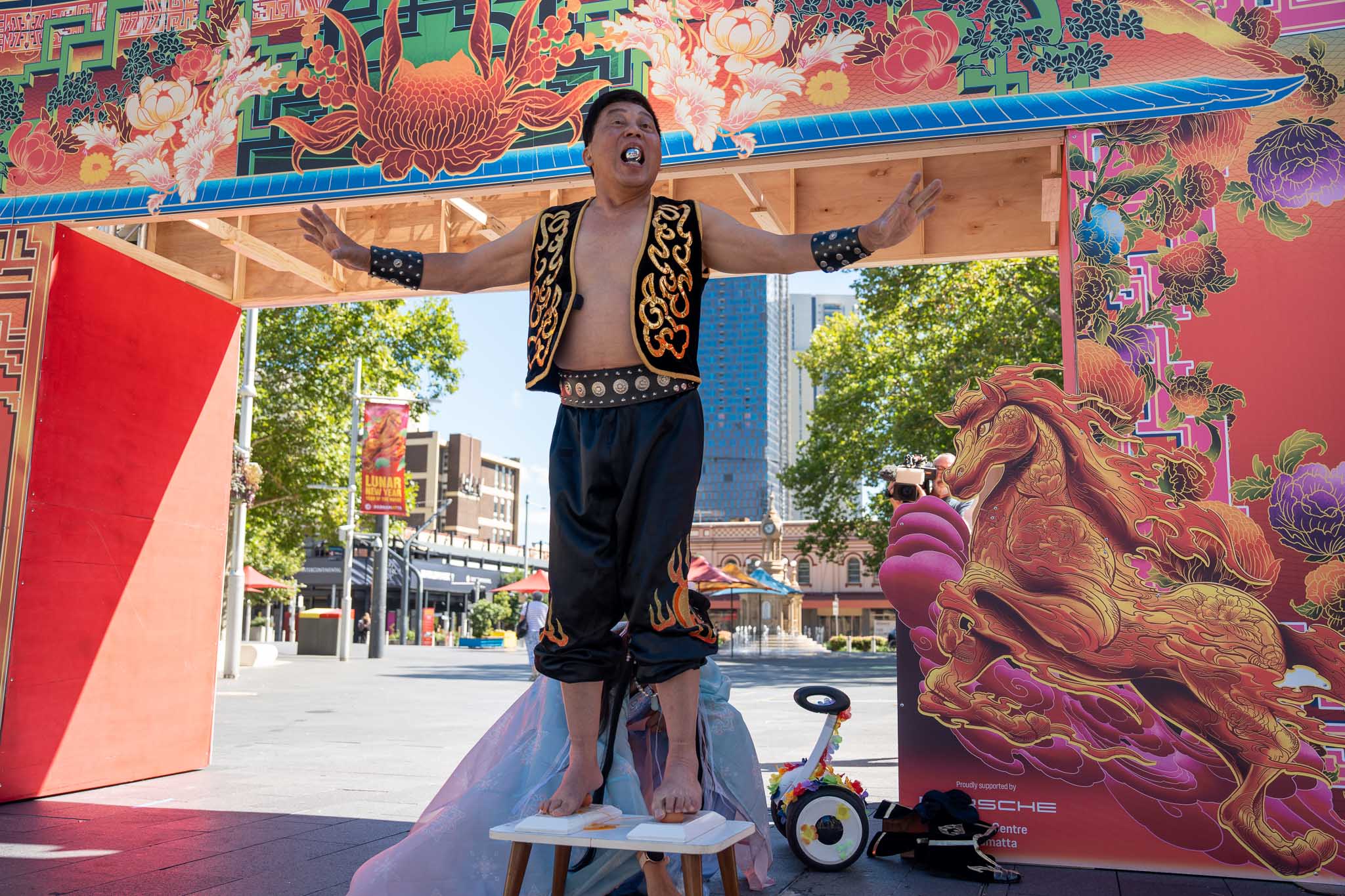 A man with a silver egg in his mouth stands on top of four eggs on a small table in front of a Lunar New Year sign.