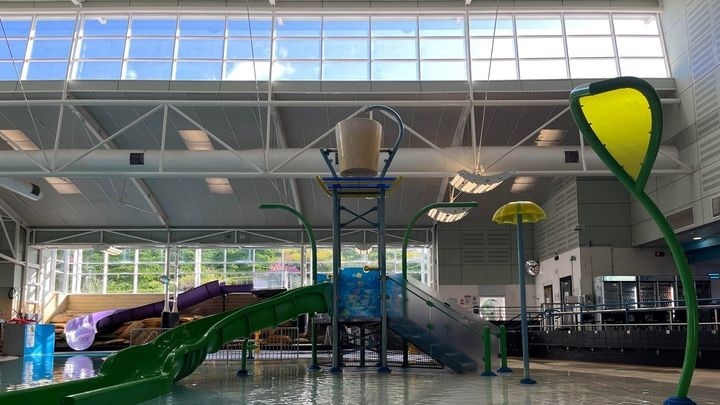 Childrens swimming pool with stair and slide structure, above is a large yellow bucket that tips when full