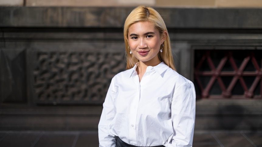 A young woman wearing a business shirt smiles as she poses for a professional profile photograph.