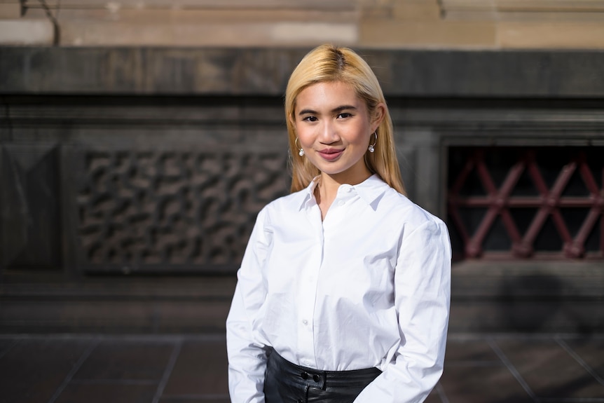 A young woman wearing a business shirt smiles as she poses for a professional profile photograph.