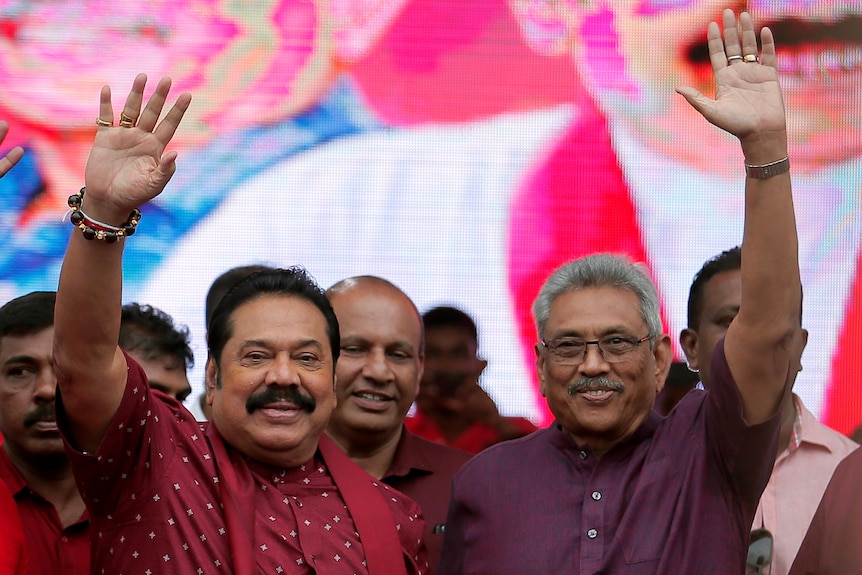 Gotabaya Rajapaksa in a purple shirt waves with his brother Mahinda Rajapaksa in red shirt and scarf, waving from a crowd