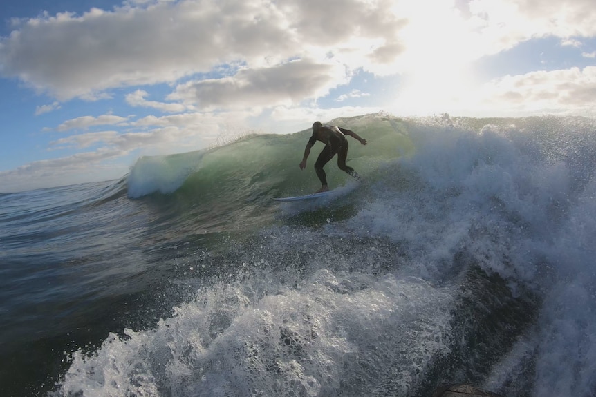 A man in a black wetsuit surfing a wave