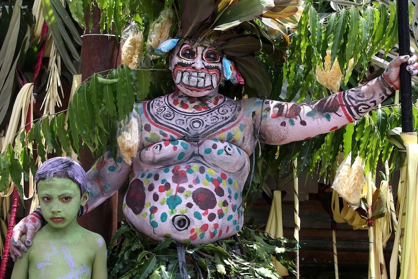A large man and his young son with painted bodies wear leaf costumes as part of a Hindu ritual to ward off evil.