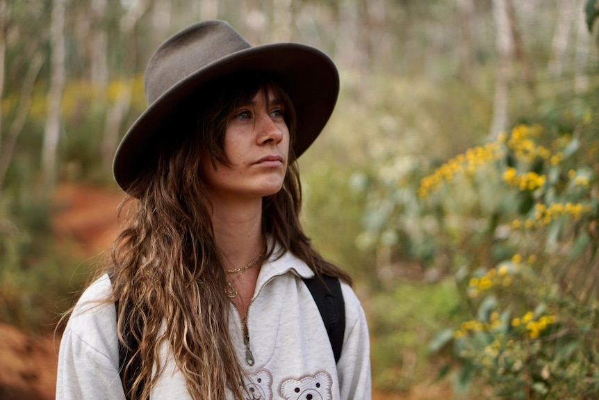 Woman wearing a white shirt and hat, standing in the bush.