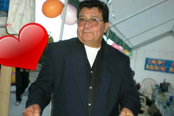 Hugo Alaniz stands posing for a photo at a birthday party indoors with a giant red heart on his right.