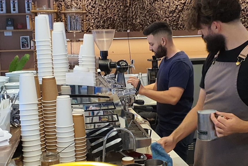 Daniel Milky stands in front of a coffee machine with another man standing next to him