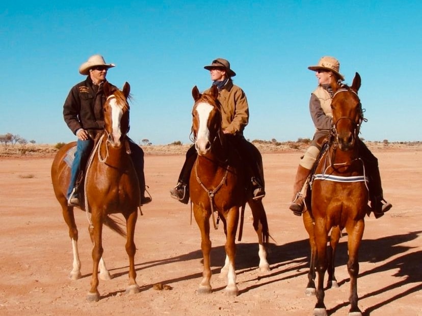 Three riders on horses in desert setting