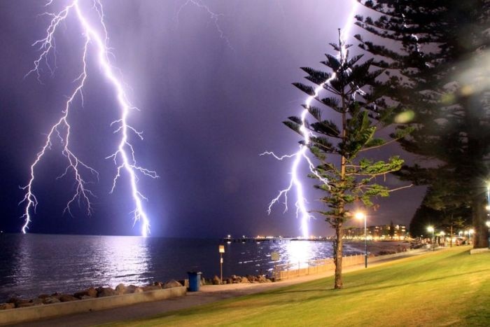 Bolts of lightning striking beyond a river.