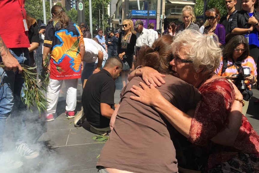 Women console each other at a smoking ceremony as tributes removed