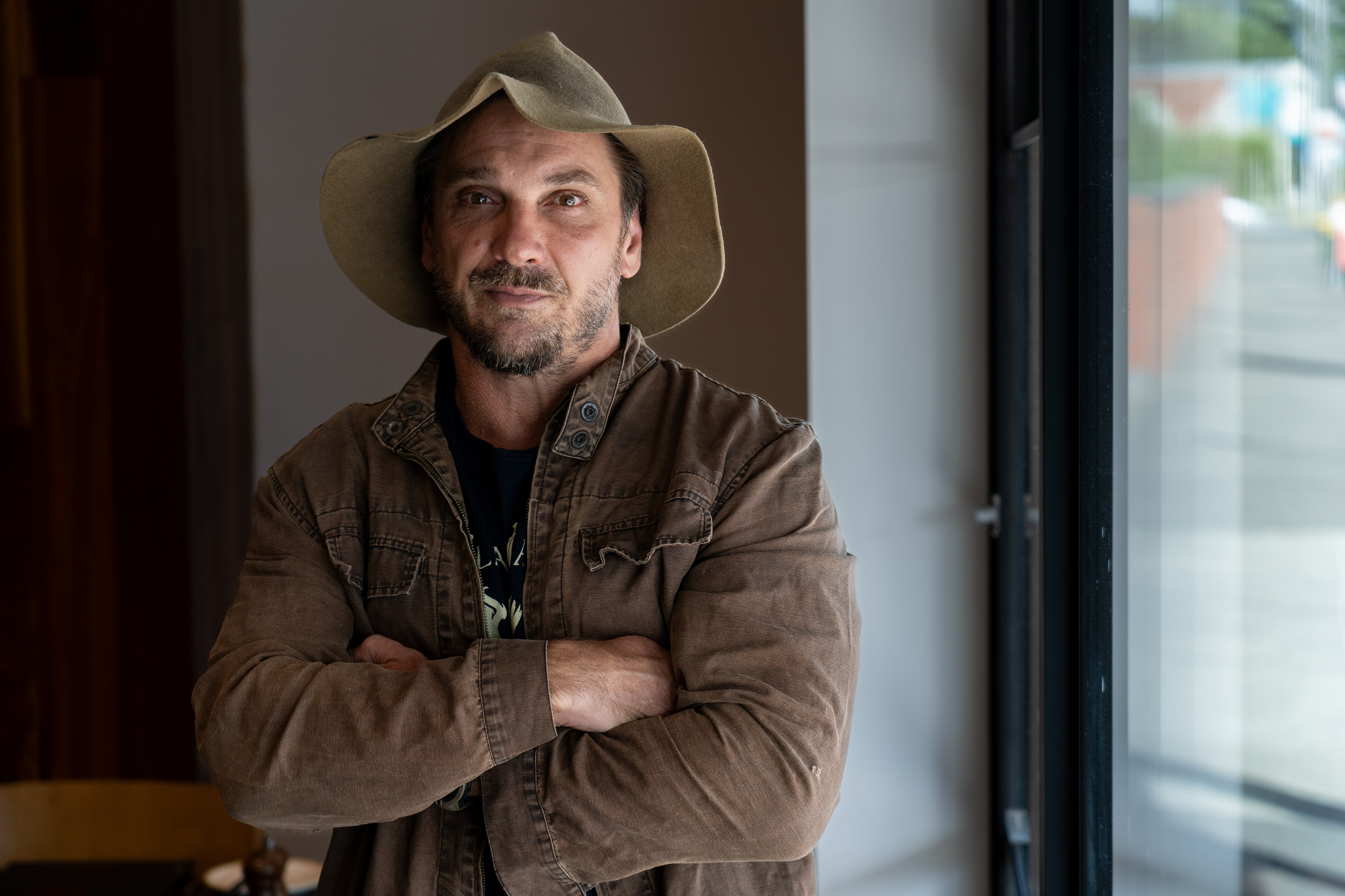 A man looks at the camera with his arms crossed wearing a hat. 