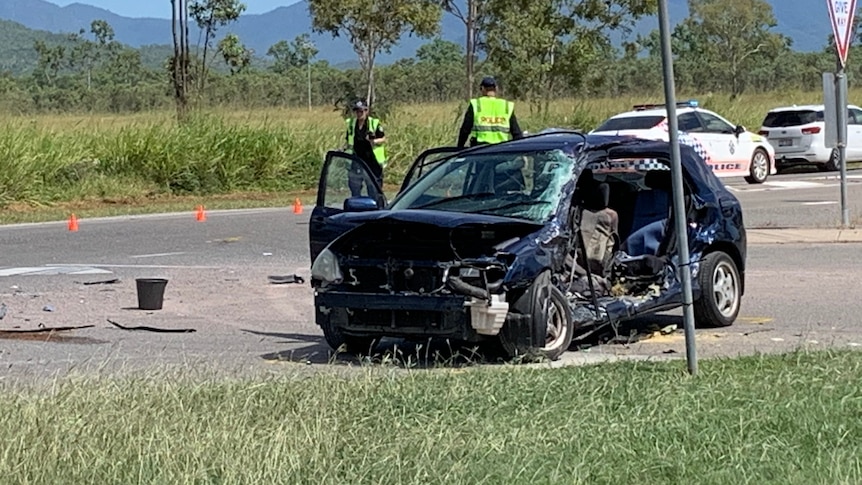 A badly wrecked car on the side of the road with two police officers nearby.