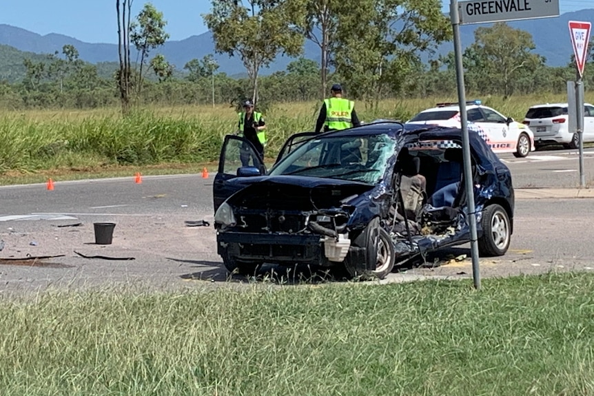 A badly wrecked car on the side of the road with two police officers nearby.