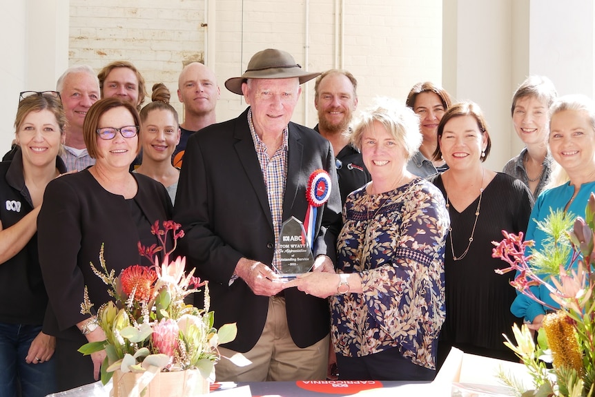 A group of people with Tom Wyatt in the center holding an award.