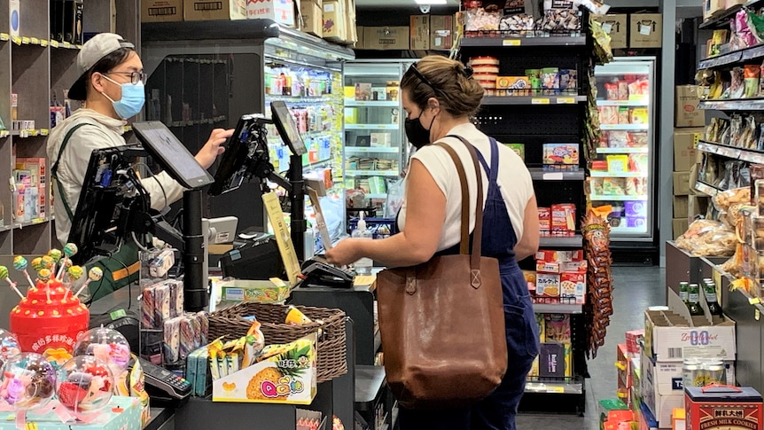 A man in a mask is serving a woman in a supermarket