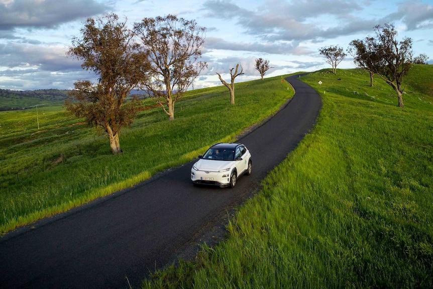 An electric car drives through green countryside.