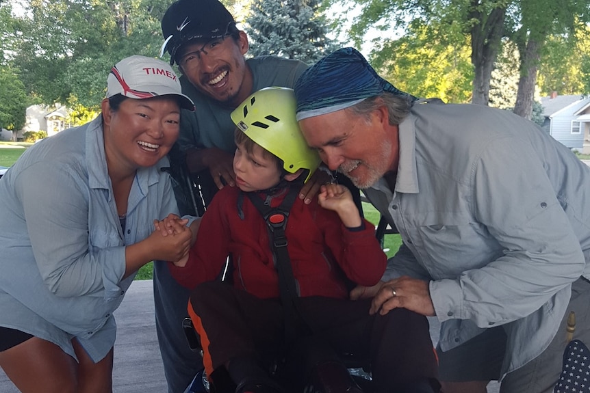 A young boy sits on a semi-recumbent bike with two men and one woman around him smiling