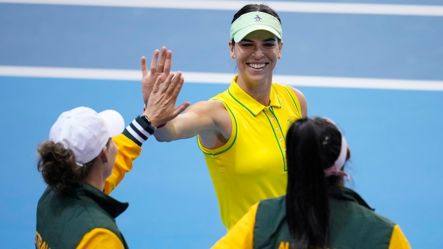 Australian tennis player Ajla Tomljanovic smiles and high-fives teammates after a win.