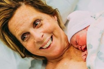 Cecile Eledge smiles lying on a hospital bed cradling her grandchild she gave birth to.