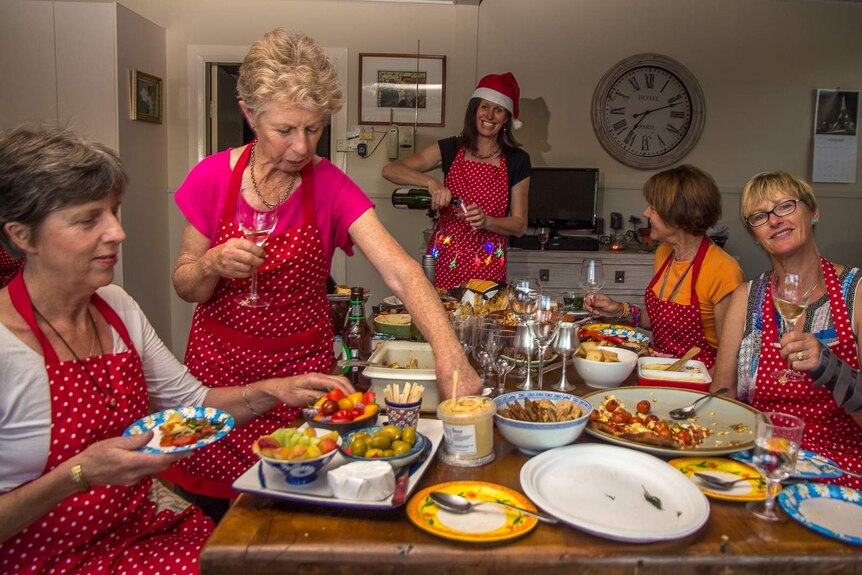 Women in red spotted aprons eat and drink around a table