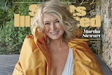 Martha Stewart, wearing short blonde hair, a white swimsuit and gold wrap, poses for a photo, smiling