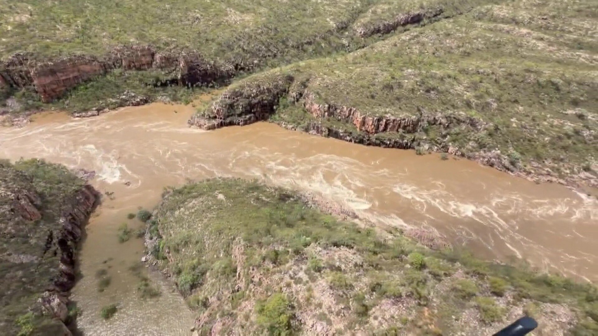 A photo of brown water rushing through a swollen gorge.