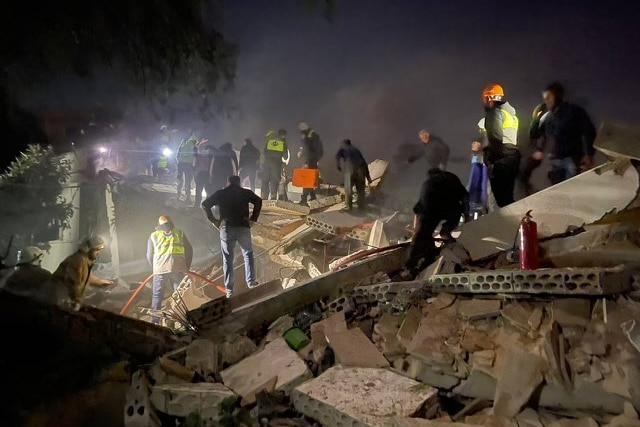Rescue workers look over a pile of rubble