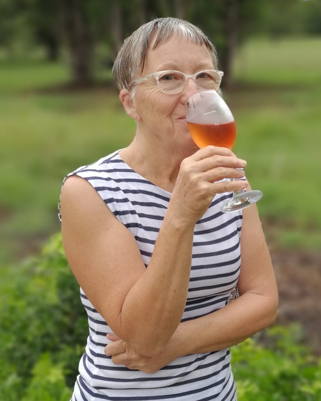 A middle aged woman standing and drinking a glass of wine. 