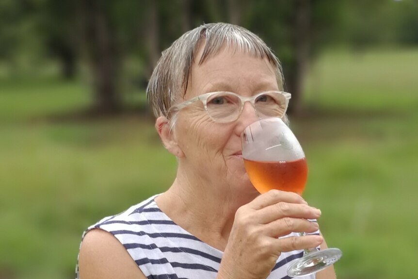 A middle aged woman standing and drinking a glass of wine. 