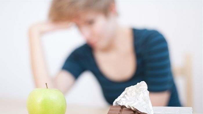 An apple and a piece of chocolate with someone in the background