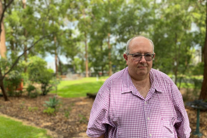 A middle-aged man in a plaid shirt walking through a park.