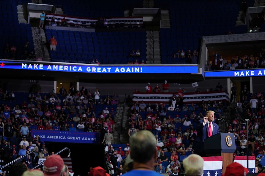 Mr Trump speaks at a podium in front of a partially filly stadium crowd