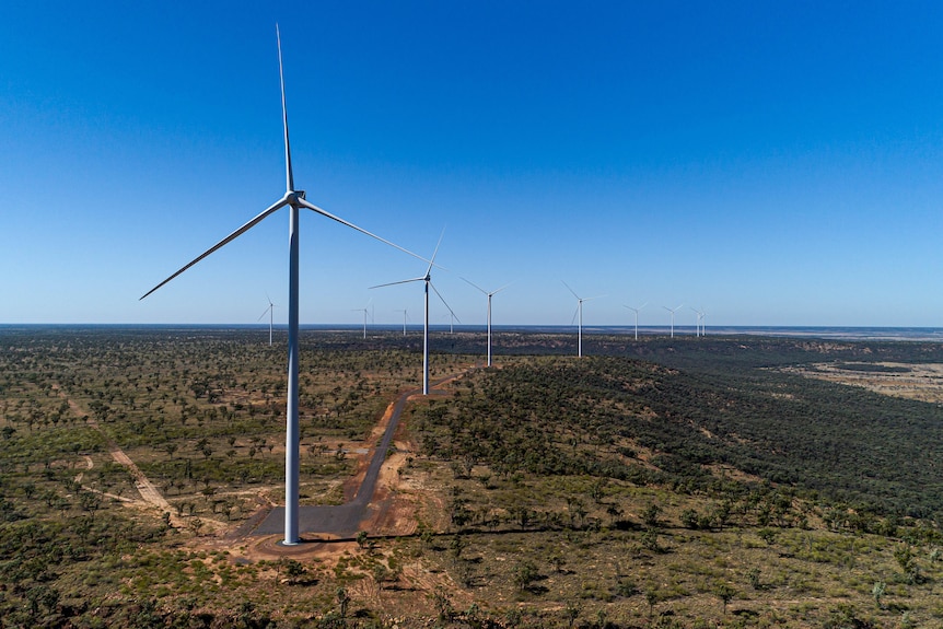 A drone shot of large wind turbines with a clear blue sky in the background