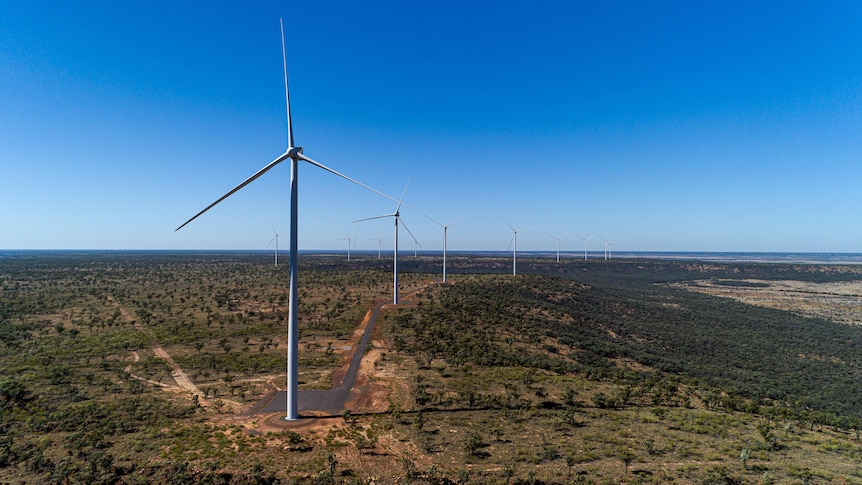 A drone shot of large wind turbines with a clear blue sky in the background