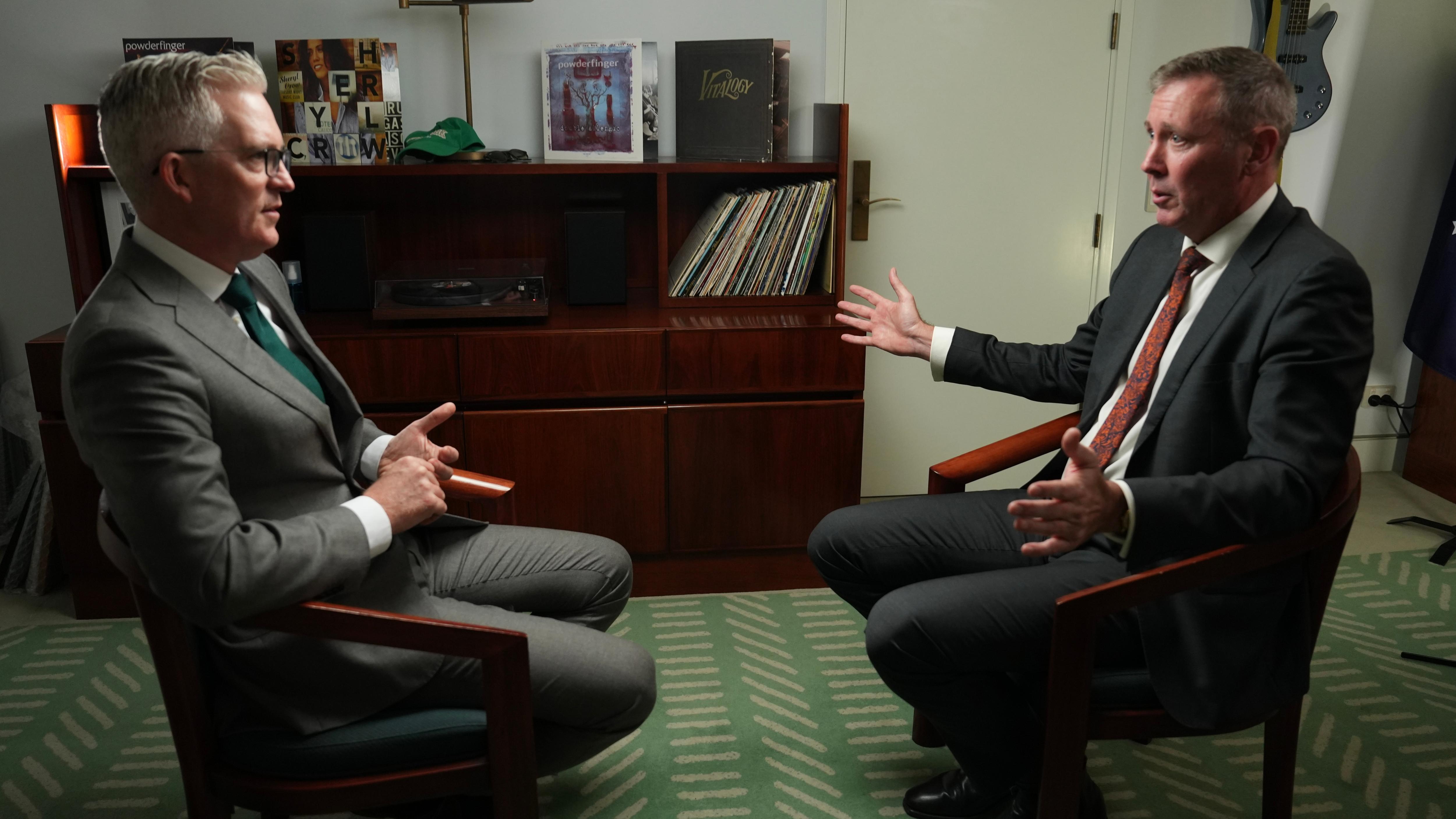 Two men in suits sitting opposite each other in chairs.