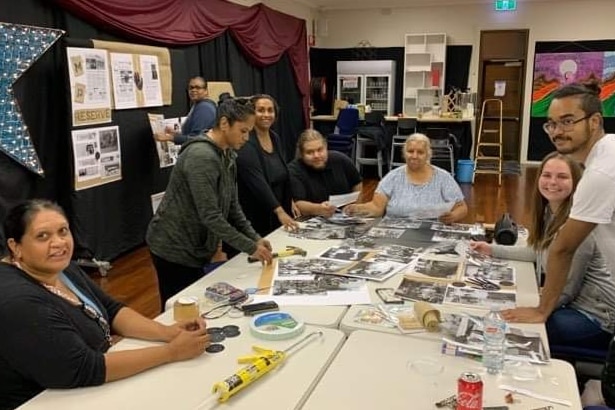 Indigenous people looking at photographs on a table with photos pinned on the wall.