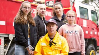 Chris Seymour sits in his yellow CFA uniform, flanked by his wife and three daughters.