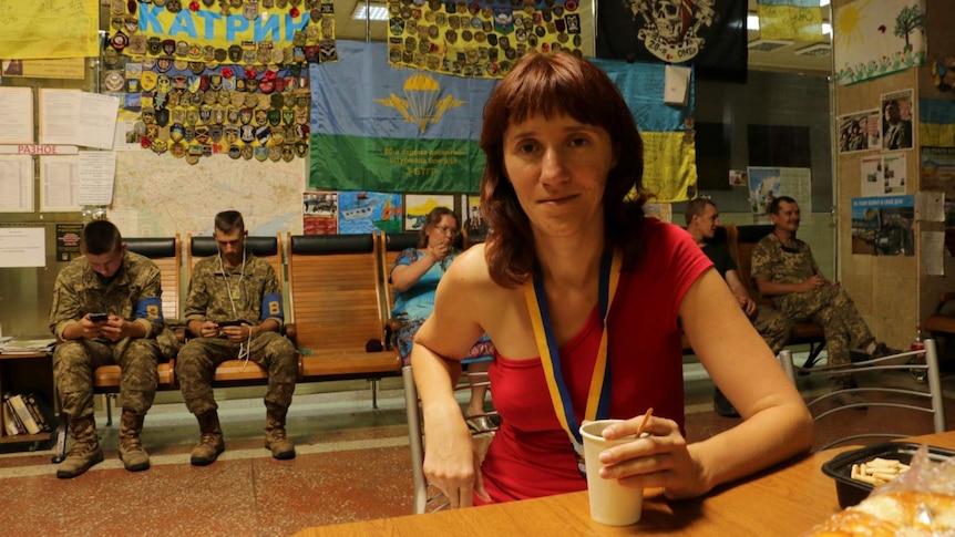 Natalia Tamarieva holding a drink, surrounded by soldiers and flags.