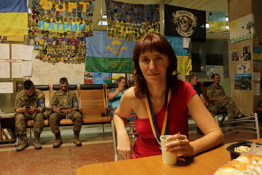 Natalia Tamarieva holding a drink, surrounded by soldiers and flags.
